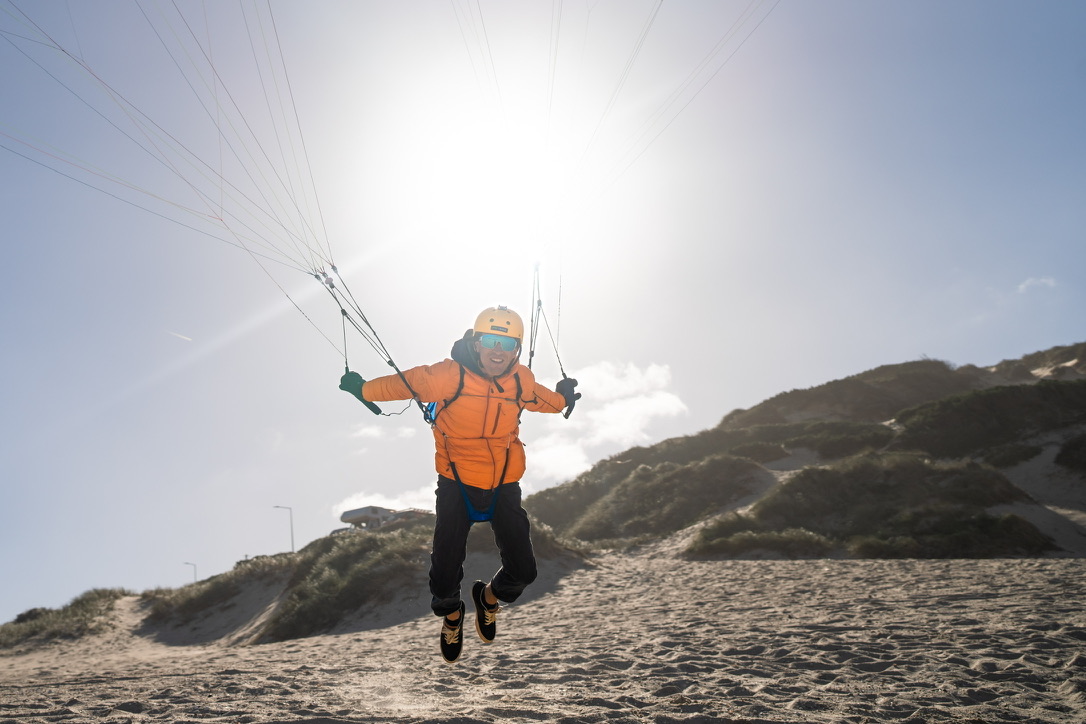 Pilot mit orangefarbener Jacke beim Schirmhandling am Strand
